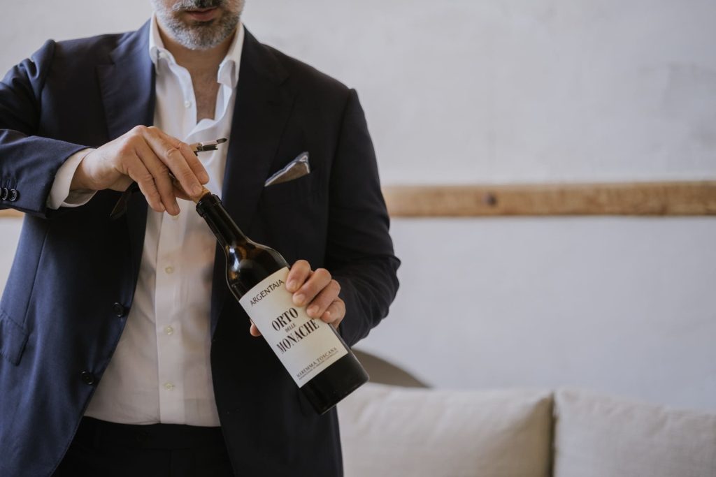 Uomo in giacca blu apre una bottiglia di vino rosso con cavatappi